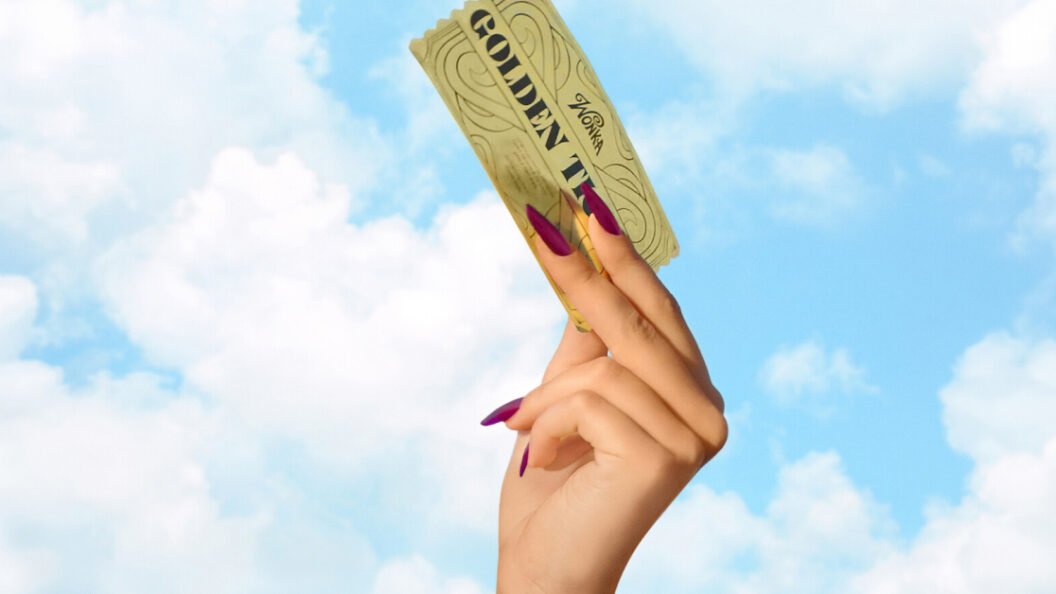 Mão erguendo o Bilhete Dourado de Willy Wonka contra um céu azul com nuvens, em referência ao reality show Wonka: O Bilhete Dourado da Netflix.